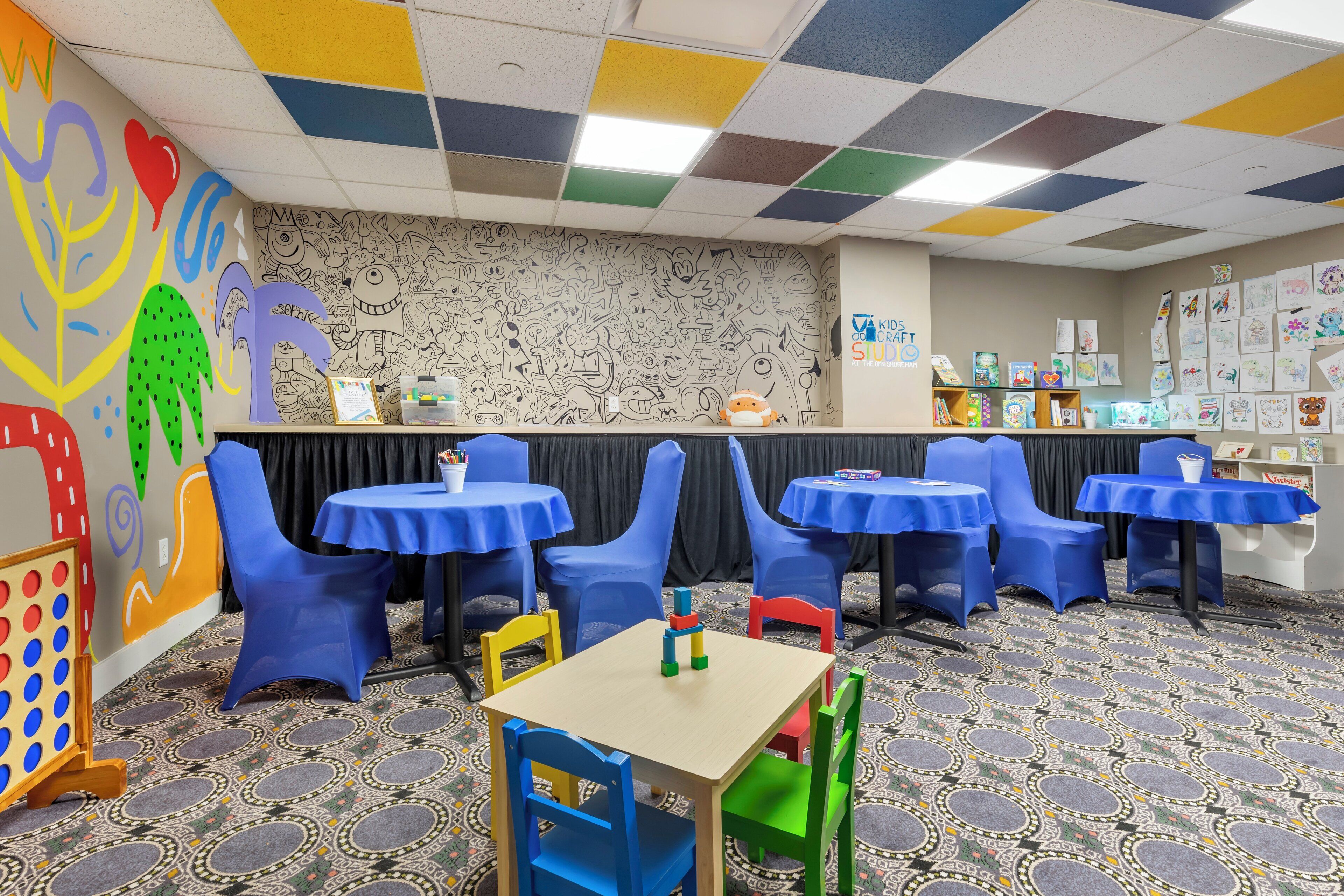 A children's activity room with colorful walls, blue plastic chairs, and tables.