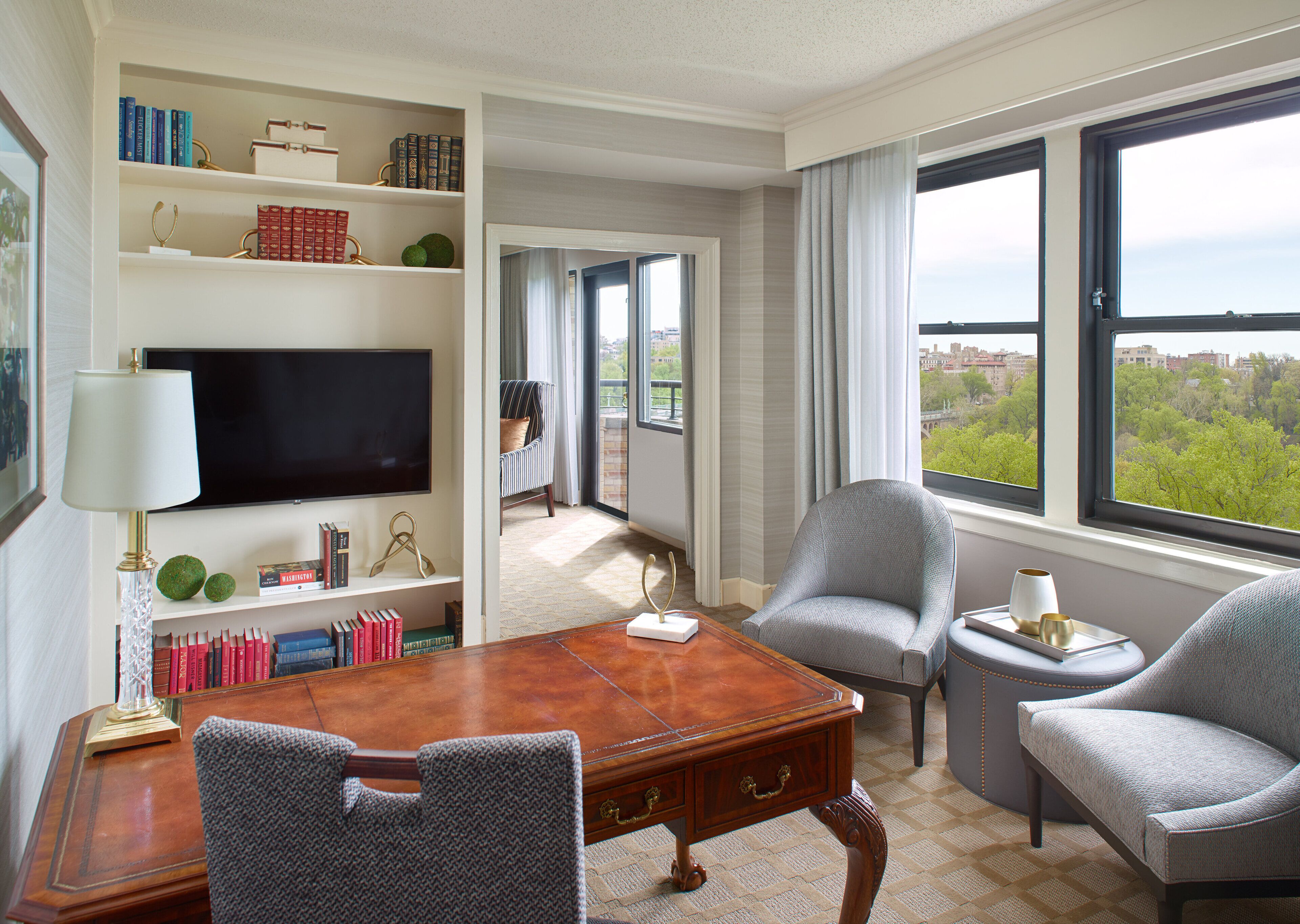 A spacious room with a large wooden desk, two armchairs, a bookshelf, and a television.