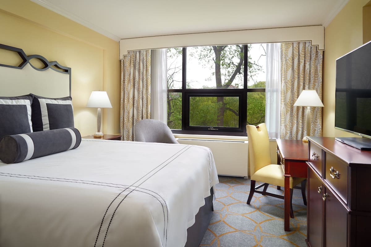 A hotel room with a large bed, a desk with a television, a chair, and a window with curtains.