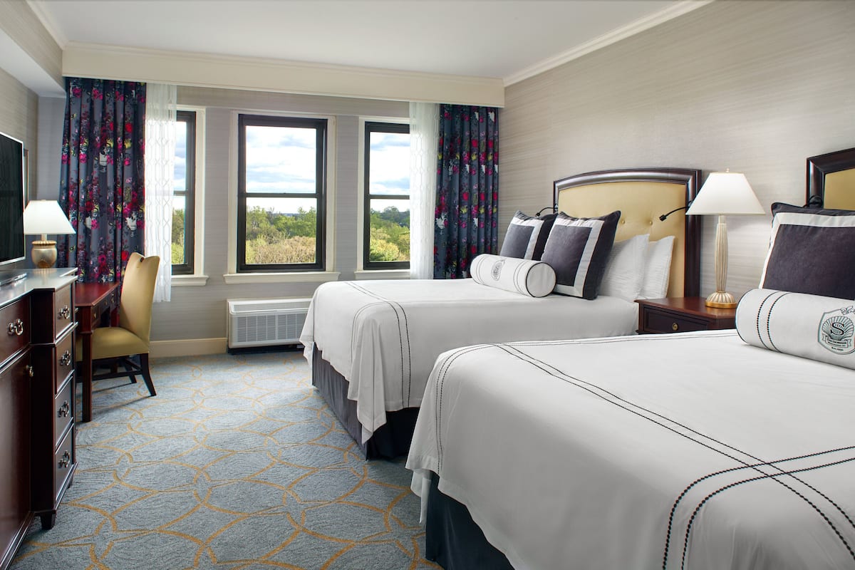 A hotel room with two beds, a desk with a television, and a chair.