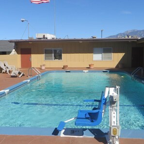 Una piscina con socorrista, sillas de descanso y un edificio con ventanas y una bandera.