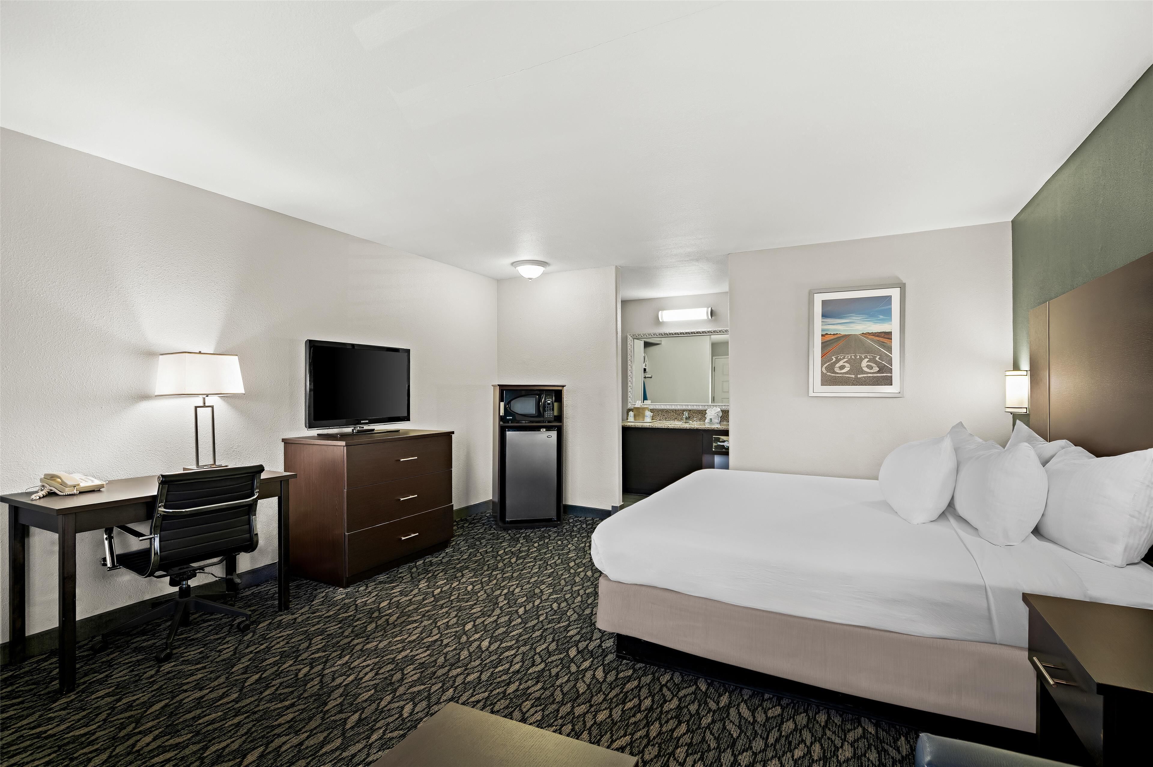 Une chambre d’hôtel équipée d’un lit, d’un bureau, d’une chaise, d’une télévision, d’un minibar et d’un tableau au mur.