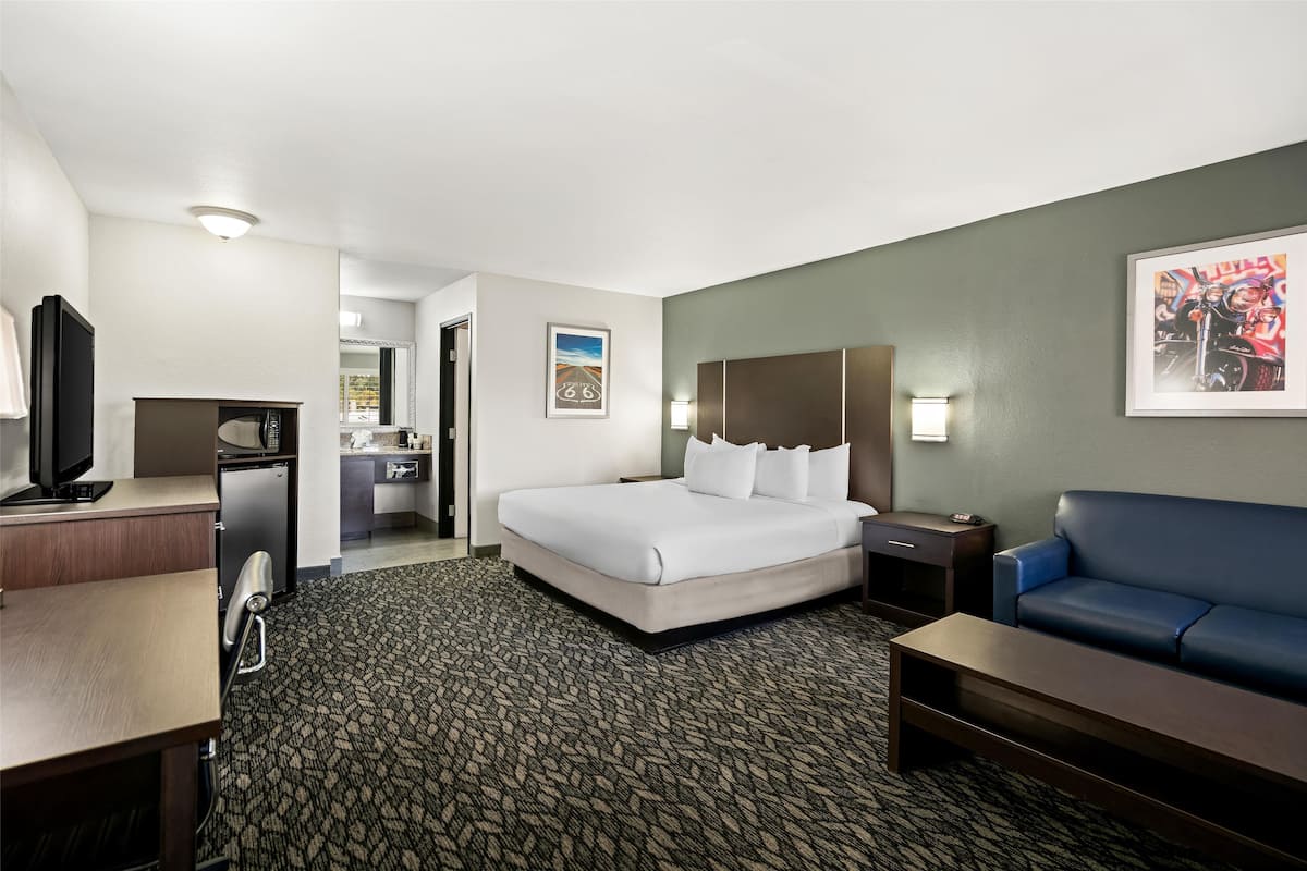 Ein Hotelzimmer mit Bett, Schreibtisch, Fernseher, Minikühlschrank, einer Couch und Teppichboden.