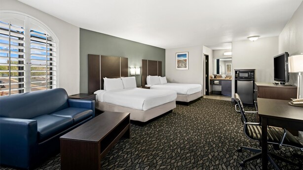 A hotel room with two beds, a sofa, a desk, a television, and a kitchenette. - Best Western Desert Villa Inn (Barstow)