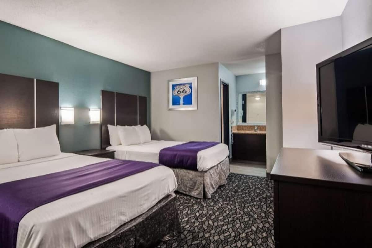 Ein Hotelzimmer mit zwei Betten, einem Schreibtisch, einem Fernseher und einem gerahmten Bild an der Wand.