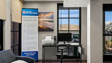 Een hotel lobby met een groot bord waarop veiligheidsafspraken staan, een bureau met een computer en uitzicht op een woestijn door een groot raam.