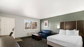 A hotel room with a bed, a desk, a chair, a sofa, a window with blinds, and a framed picture on the wall.