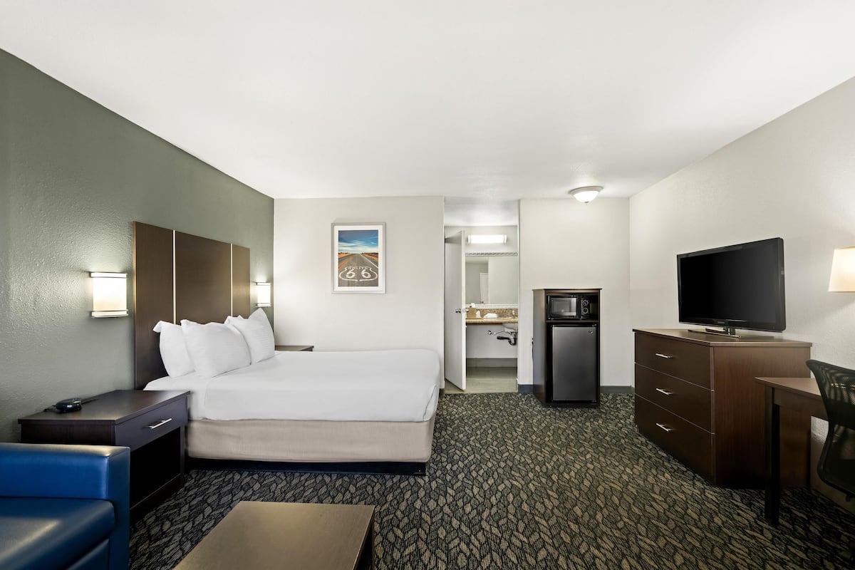 Ein Hotelzimmer mit einem Bett, einem Schreibtisch, einem Fernseher, einem Sessel, einer Schreibtischlampe, einer Mikrowelle und einer kleinen Küchenzeile.