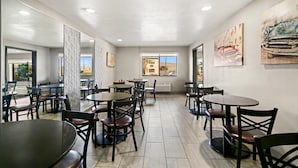 A spacious indoor dining area with multiple tables and chairs, large windows offering a view of the outside, and artwork on the walls. - Best Western Desert Villa Inn (Barstow)