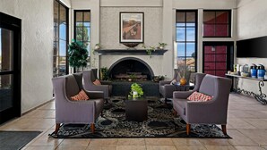 A spacious living room with a fireplace, comfortable seating, and large windows. - Best Western Desert Villa Inn (Barstow)