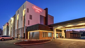 Un hotel Hampton Inn amb disseny modern, amb un cartell de neó, una zona de pàrquing coberta i una entrada ben il·luminada.