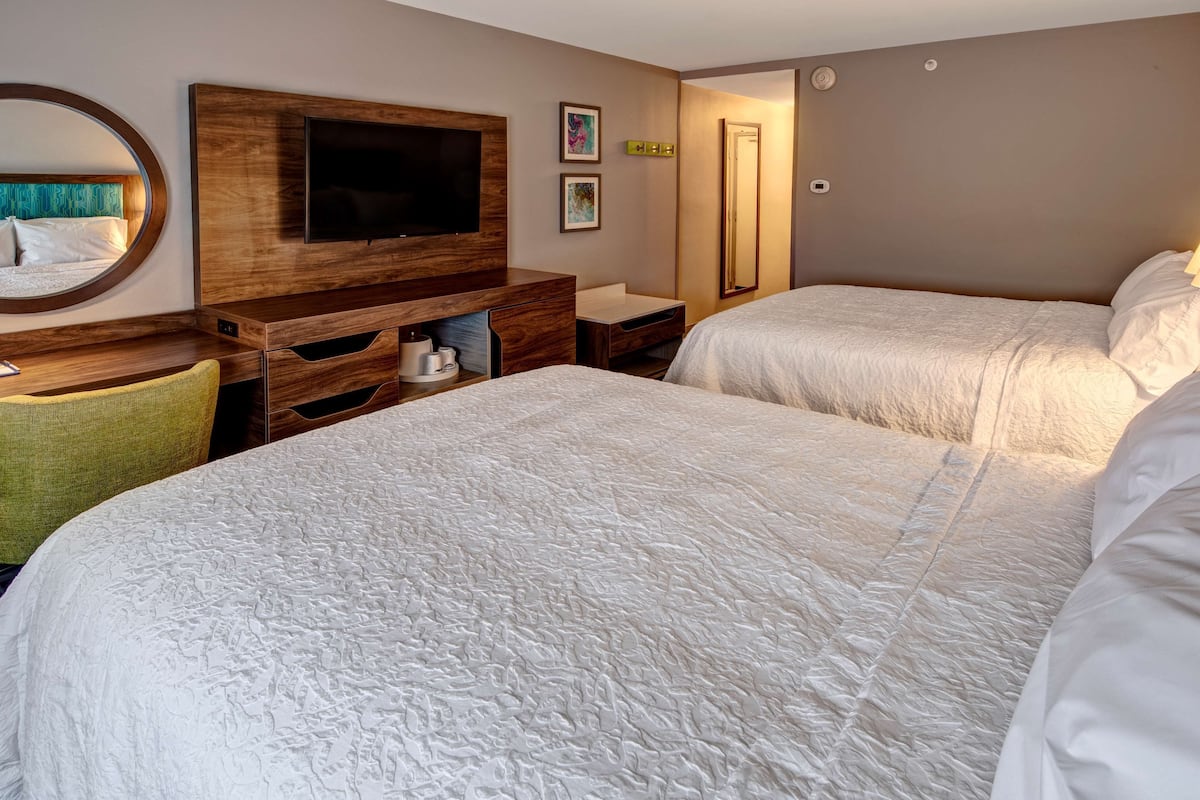 Una habitación de hotel con dos camas, televisión, escritorio y espejo.