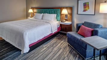 Hotellihuone, jossa on suuri sänky, sininen sohva, pieni pöytä ja yöpöytä, jossa on lamppu.