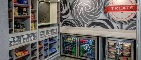 Una sección de aperitivos y dulces con estantes llenos de papas fritas, bocadillos y un refrigerador con bebidas y helados.