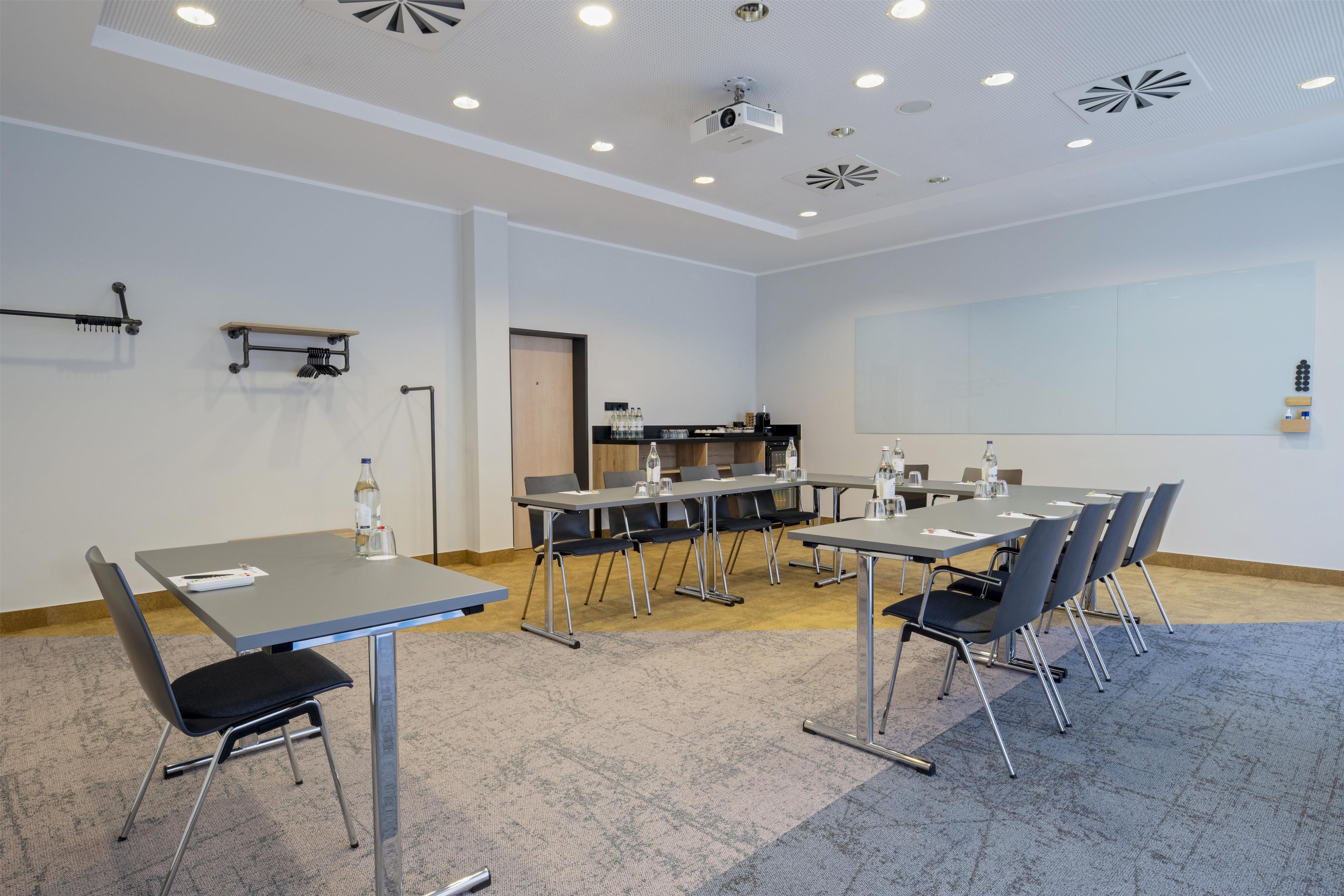 Ein Konferenzraum mit einem großen Tisch, Stühlen, einem Projektor und einer Whiteboard-Tafel.