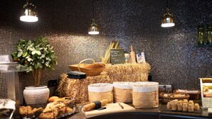 Un bufé de desayuno con diversos alimentos y recipientes, que incluyen pan, bollería y una planta.
