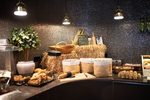 A breakfast buffet with various food items and containers, including bread, pastries, and a plant.