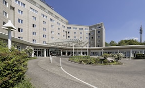 Un hotel moderno con entrada cubierta, varios pisos y una torre destacada al fondo.