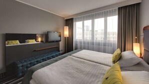 Habitación de hotel con dos camas, un televisor, un banco y un amplio ventanal con cortinas.