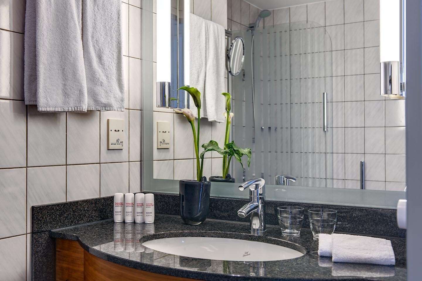 A modern bathroom with a granite countertop, a sink, a mirror, and a shower area.