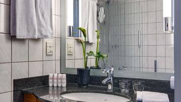 A modern bathroom with a granite countertop, a sink, a mirror, and a shower area.