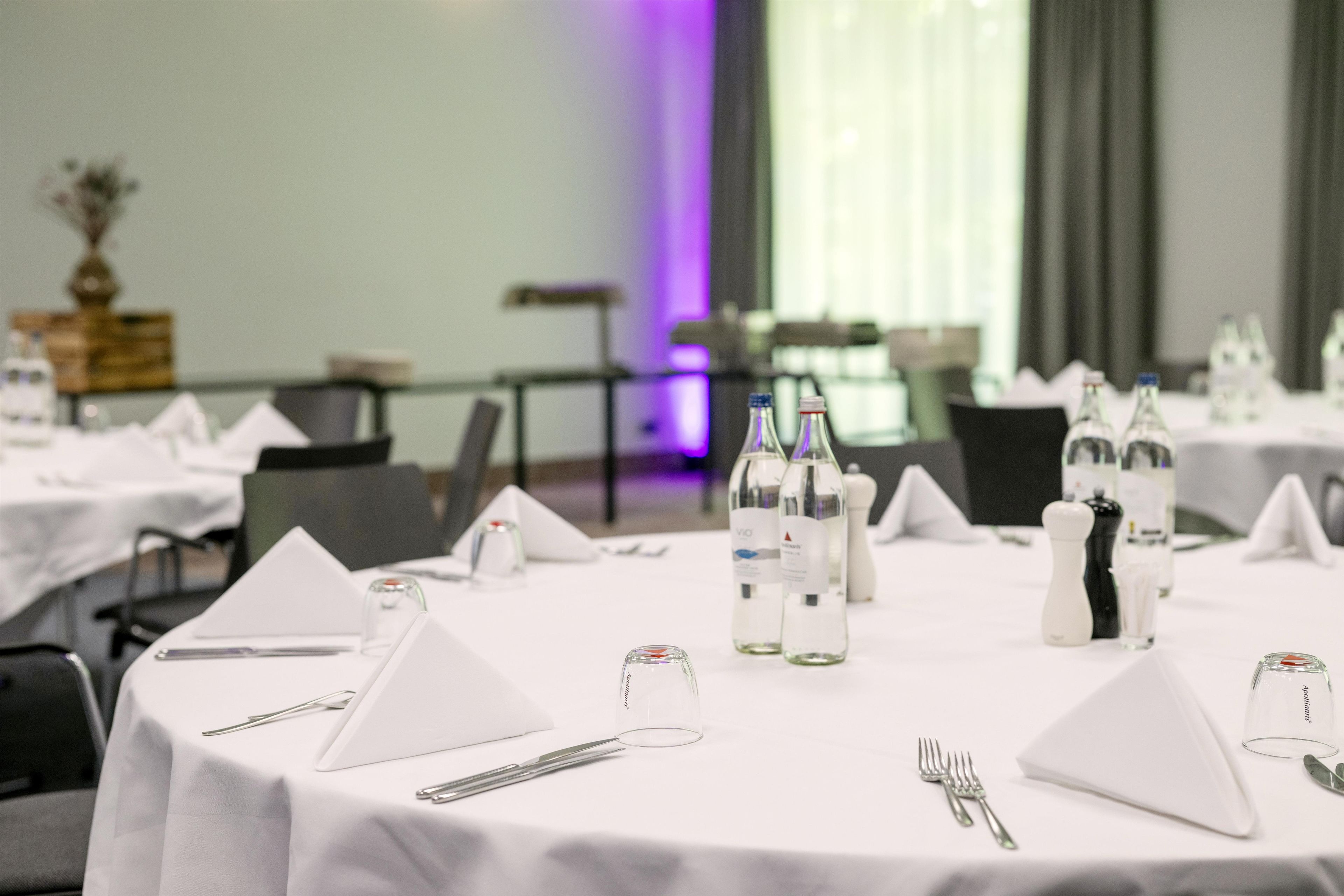A dining table set with white tablecloths, silverware, and clear glassware.