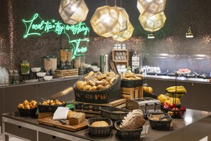 Un bufé con panes y pasteles variados, un tostador y un letrero de neón al fondo.