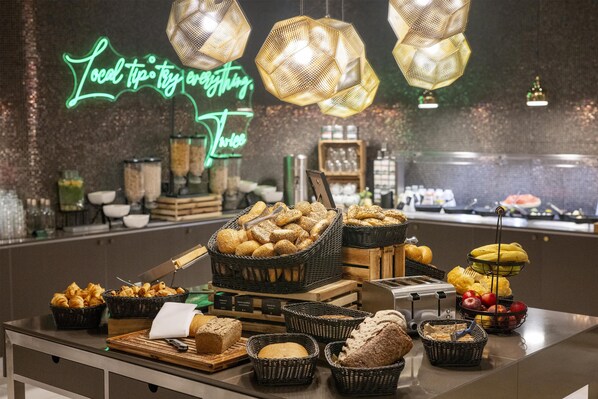 A buffet with various breads and pastries, a toaster, and a neon sign in the background.