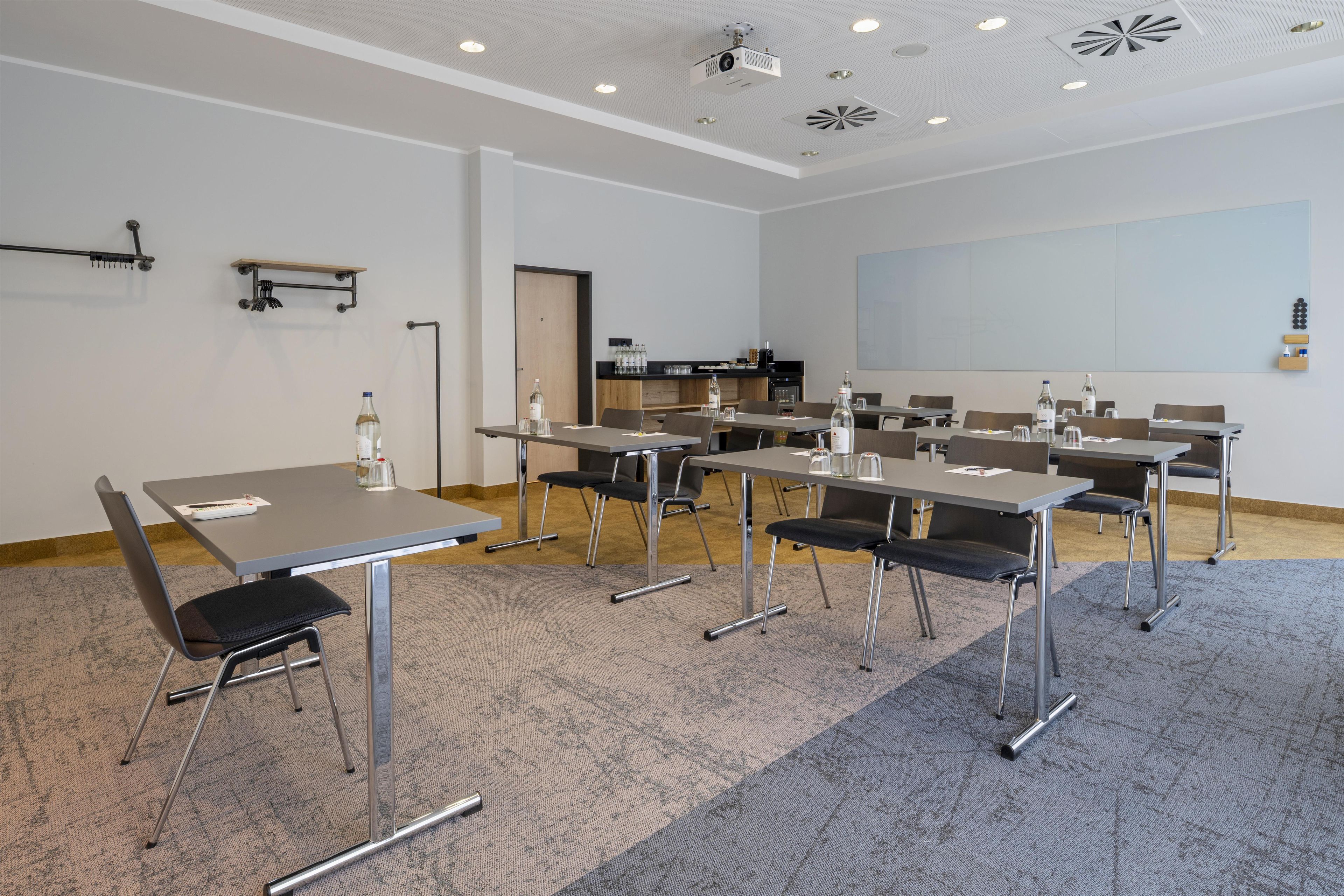 Une salle de conférence équipée de plusieurs tables et chaises, d’un projecteur et d’un grand écran mural.