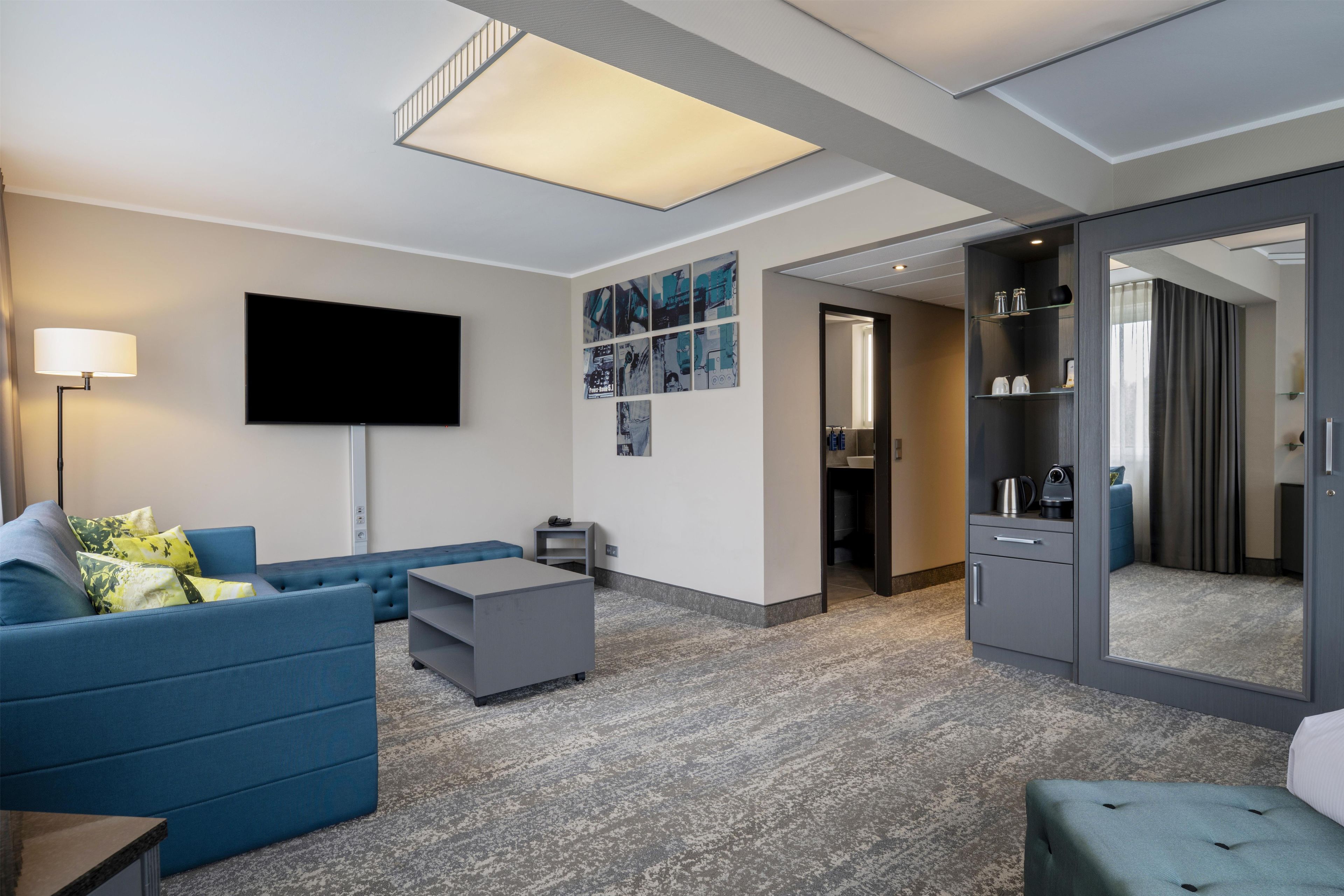 A modern hotel room with a flat-screen TV, a sofa, a coffee table, and a wardrobe.