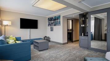 A modern hotel room with a flat-screen TV, a sofa, a coffee table, and a wardrobe.