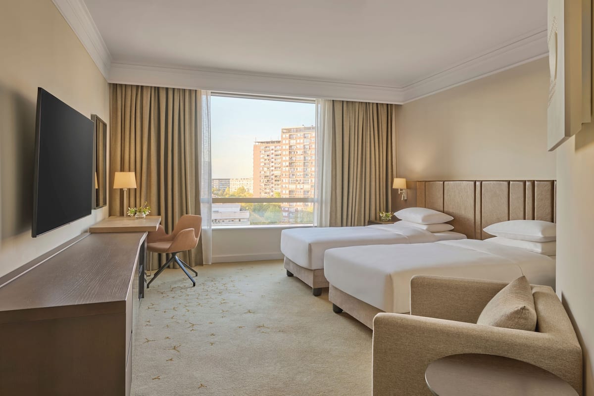 A hotel room with two beds, a desk, a chair, a TV, and a window with curtains.