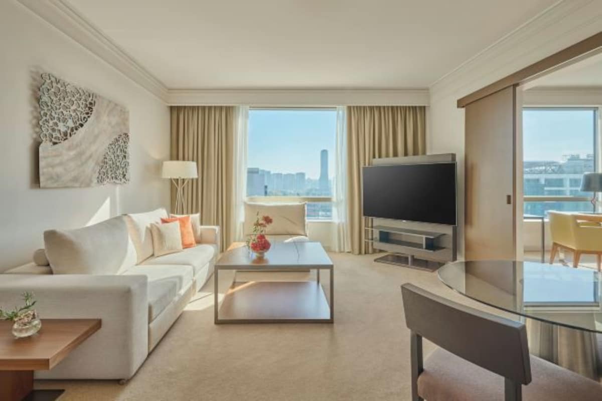 A modern hotel room with a sofa, a coffee table, a TV, and a glass dining table.