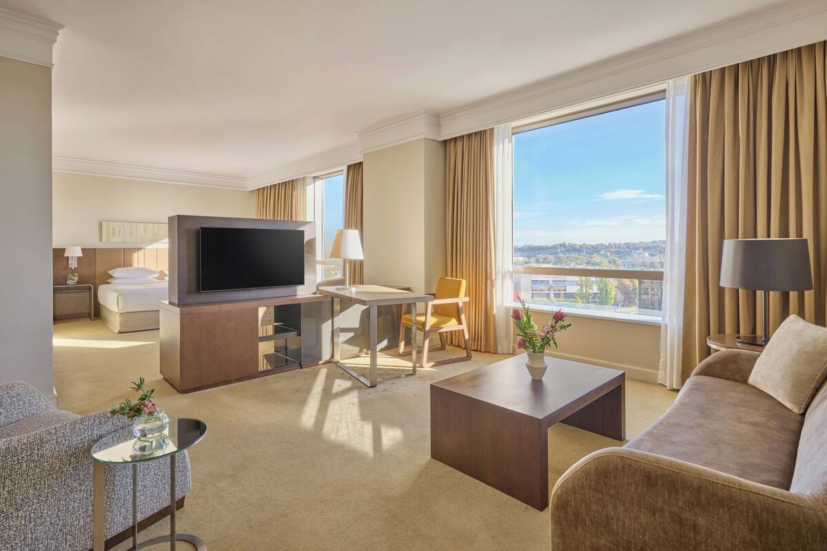 A hotel room with a TV, sofa, armchair, and a dining area with a table and chairs.