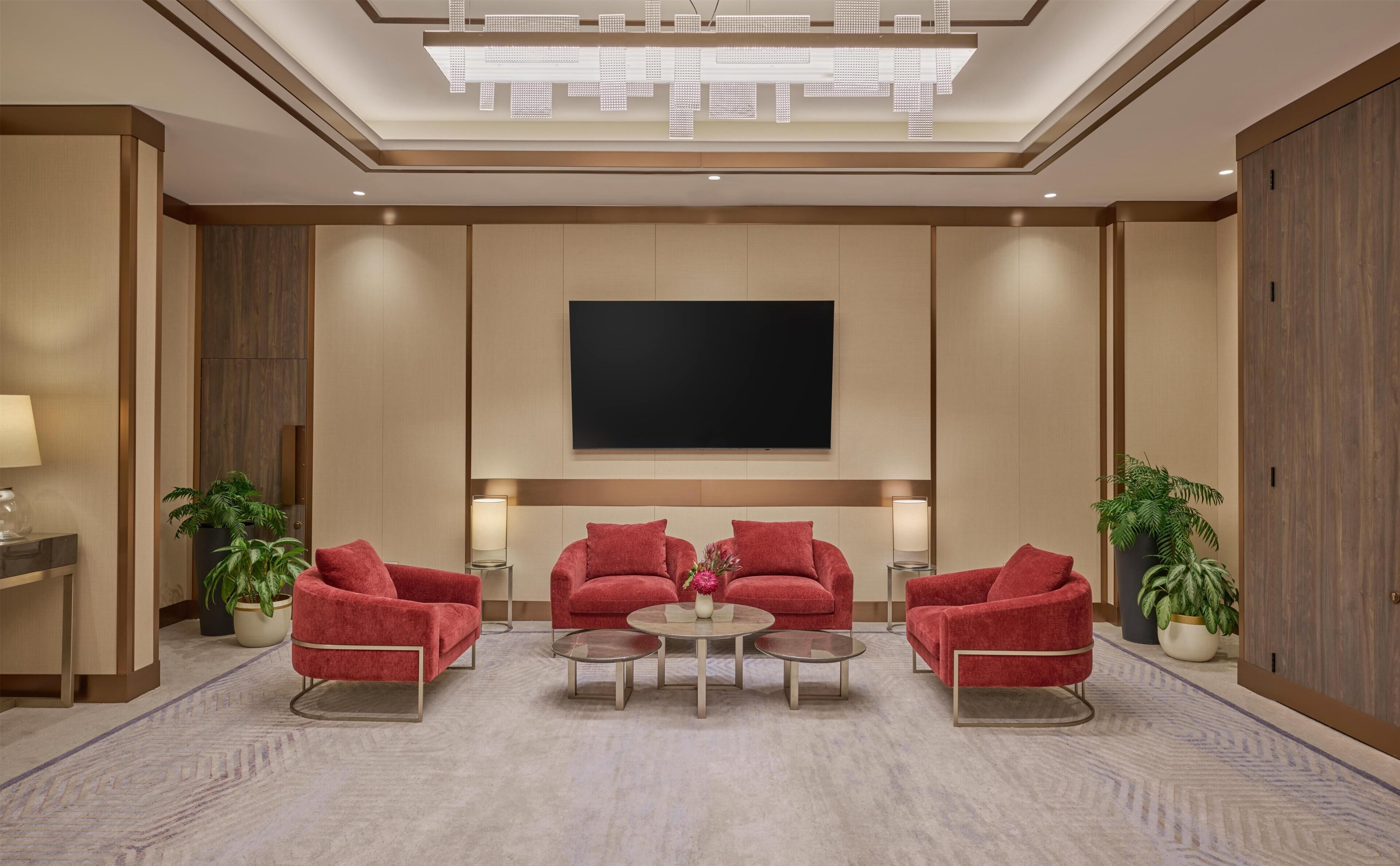 A modern living room with a flat-screen TV, red armchairs, a coffee table, and potted plants.