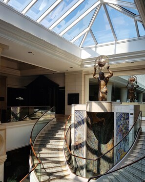 A spacious atrium with a glass ceiling, a central staircase, and a decorative sculpture.