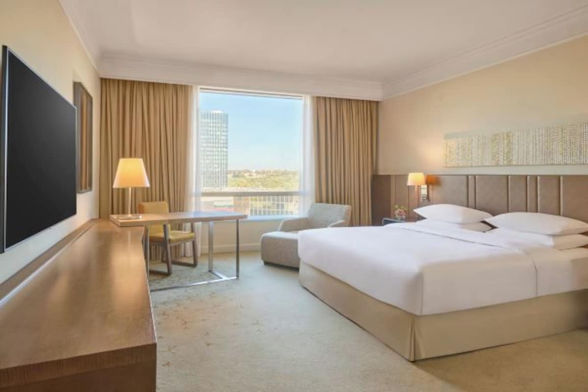 A hotel room with a bed, a desk, a chair, a TV, and a window with curtains.