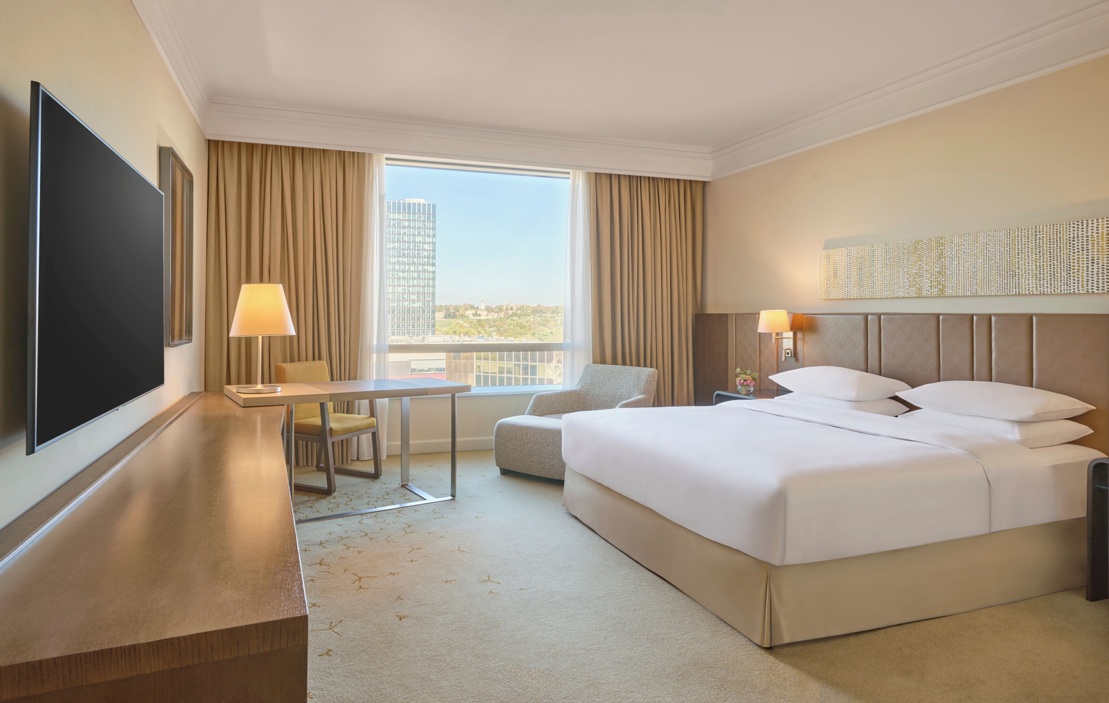 Une chambre d’hôtel avec un lit, un bureau, une chaise, une télévision et une grande fenêtre avec des rideaux.
