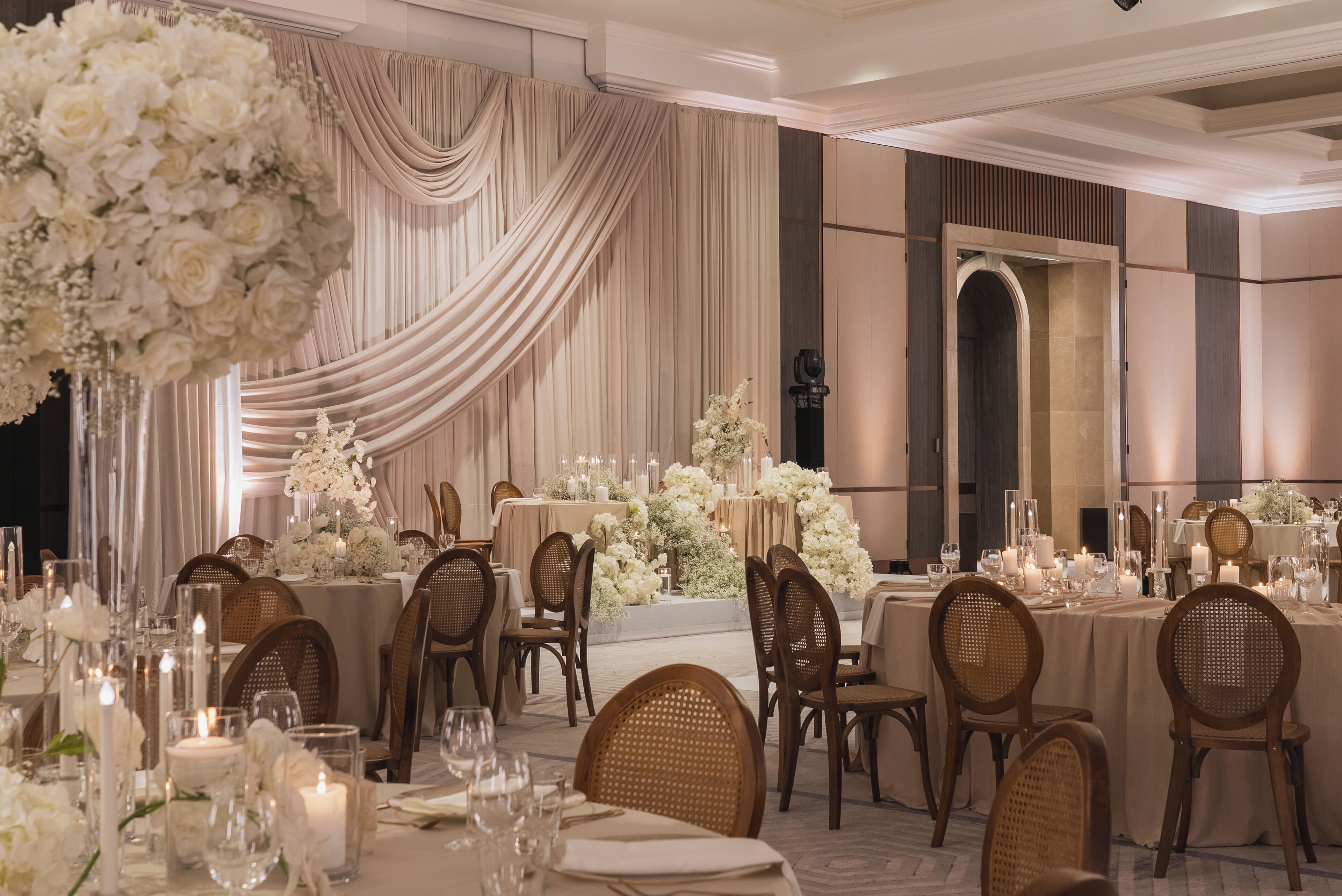 A banquet hall with round tables, chairs, and floral centerpieces.