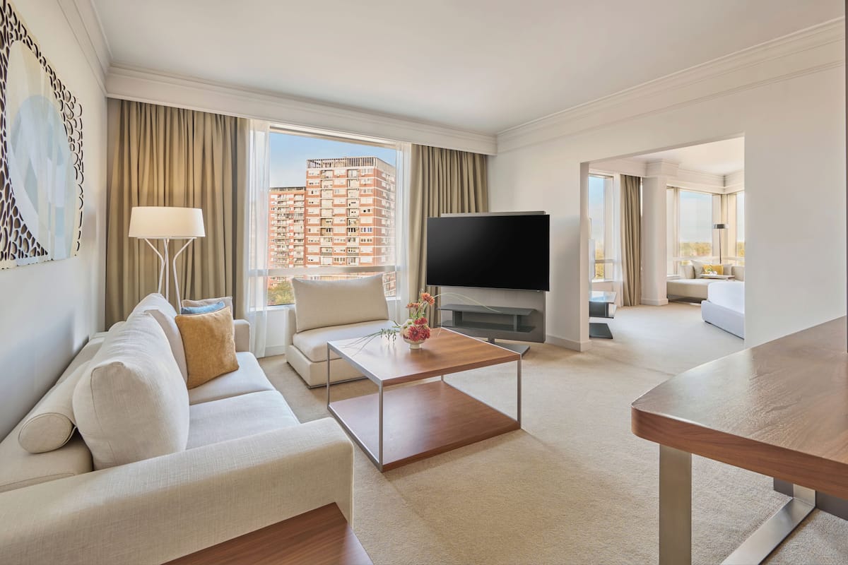 A modern hotel room with a sofa, coffee table, TV, and a view of a high-rise building.