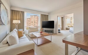 A modern hotel room with a sofa, coffee table, TV, and a view of a high-rise building. - Hyatt Regency Belgrade (Belgrade)