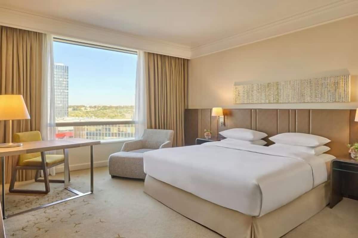 A hotel room with a large bed, a desk, a chair, and a view of the cityscape.