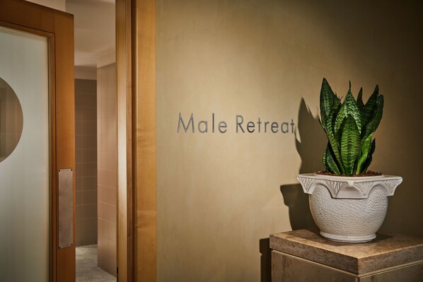 A reception area with a potted plant on a marble pedestal, a wall with the text "Male Retreat".