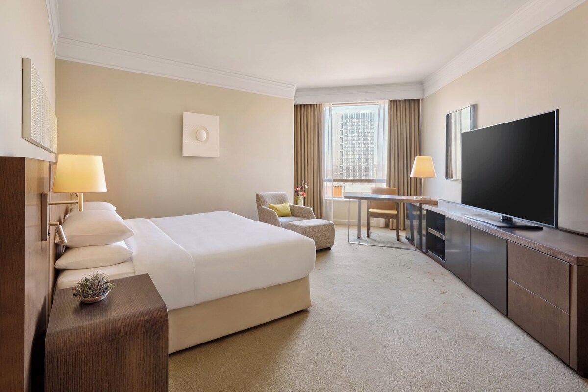 A hotel room with a bed, a desk, a television, and a window with curtains.