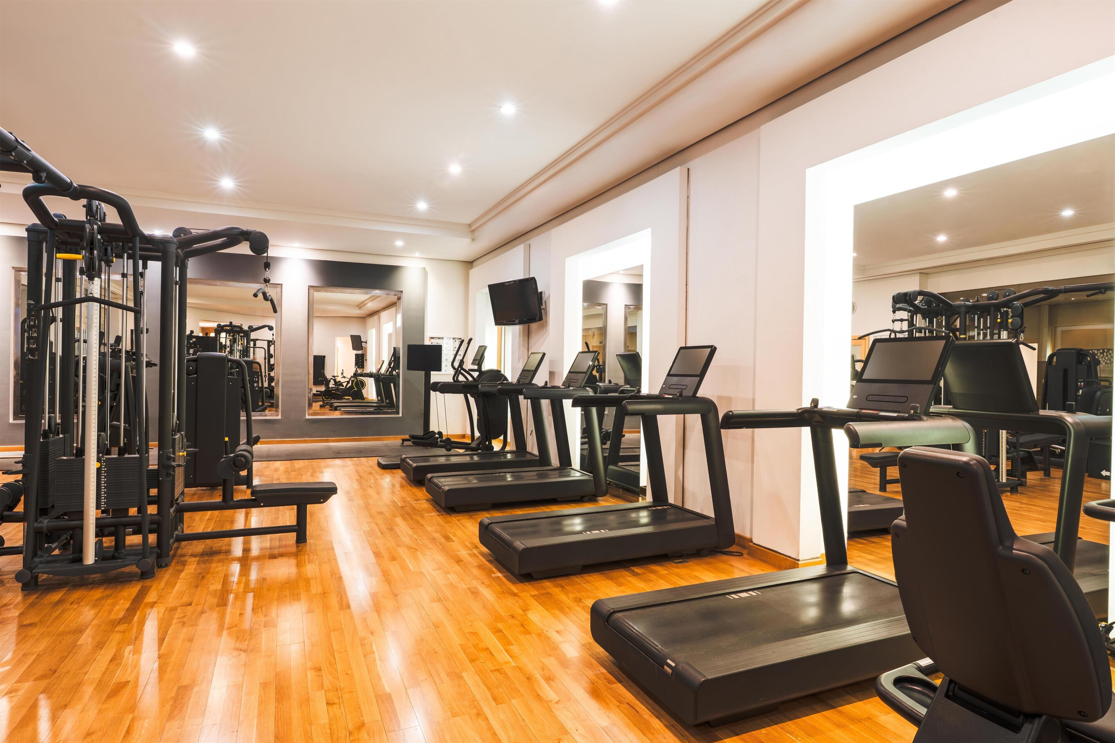 A gym with treadmills, weight machines, and a mirror wall.