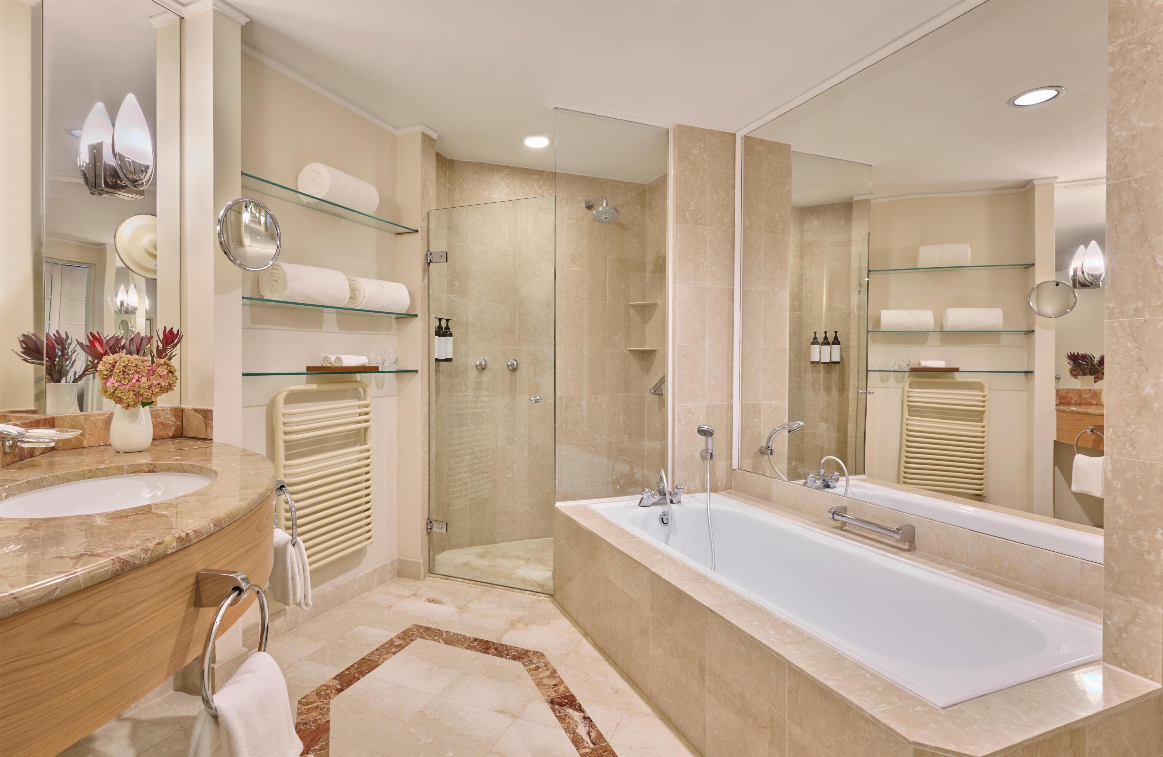 Un baño moderno con una bañera grande, cabina de ducha con mampara de cristal y varios estantes con toallas.