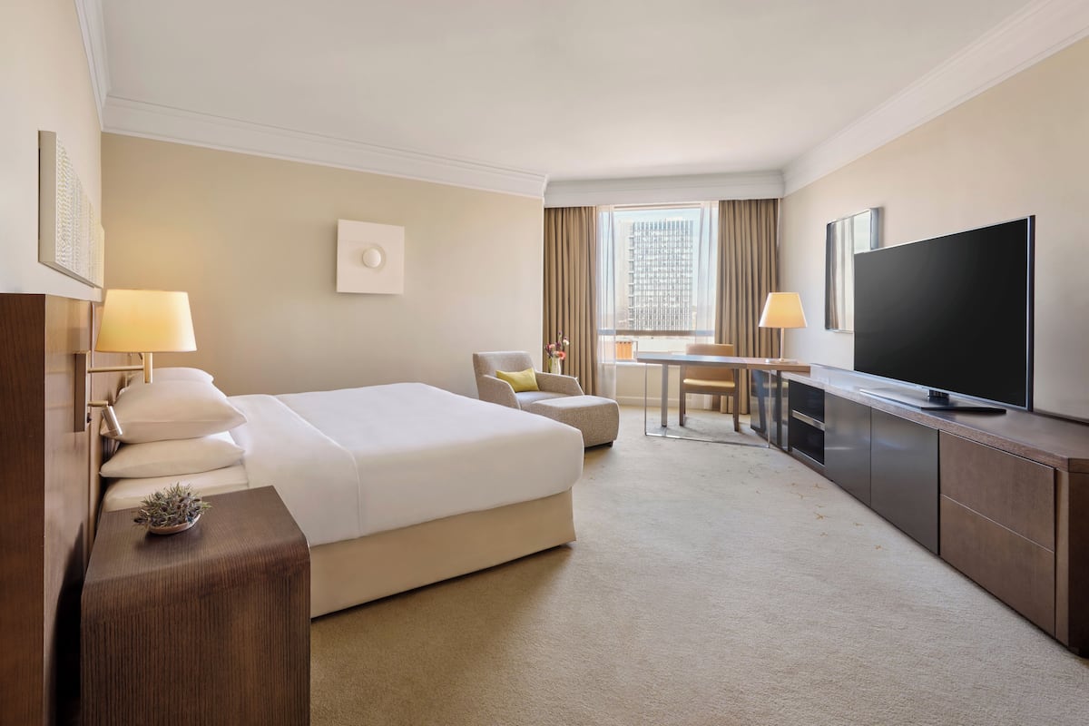 A hotel room with a large bed, a desk, a television, and a window with curtains.