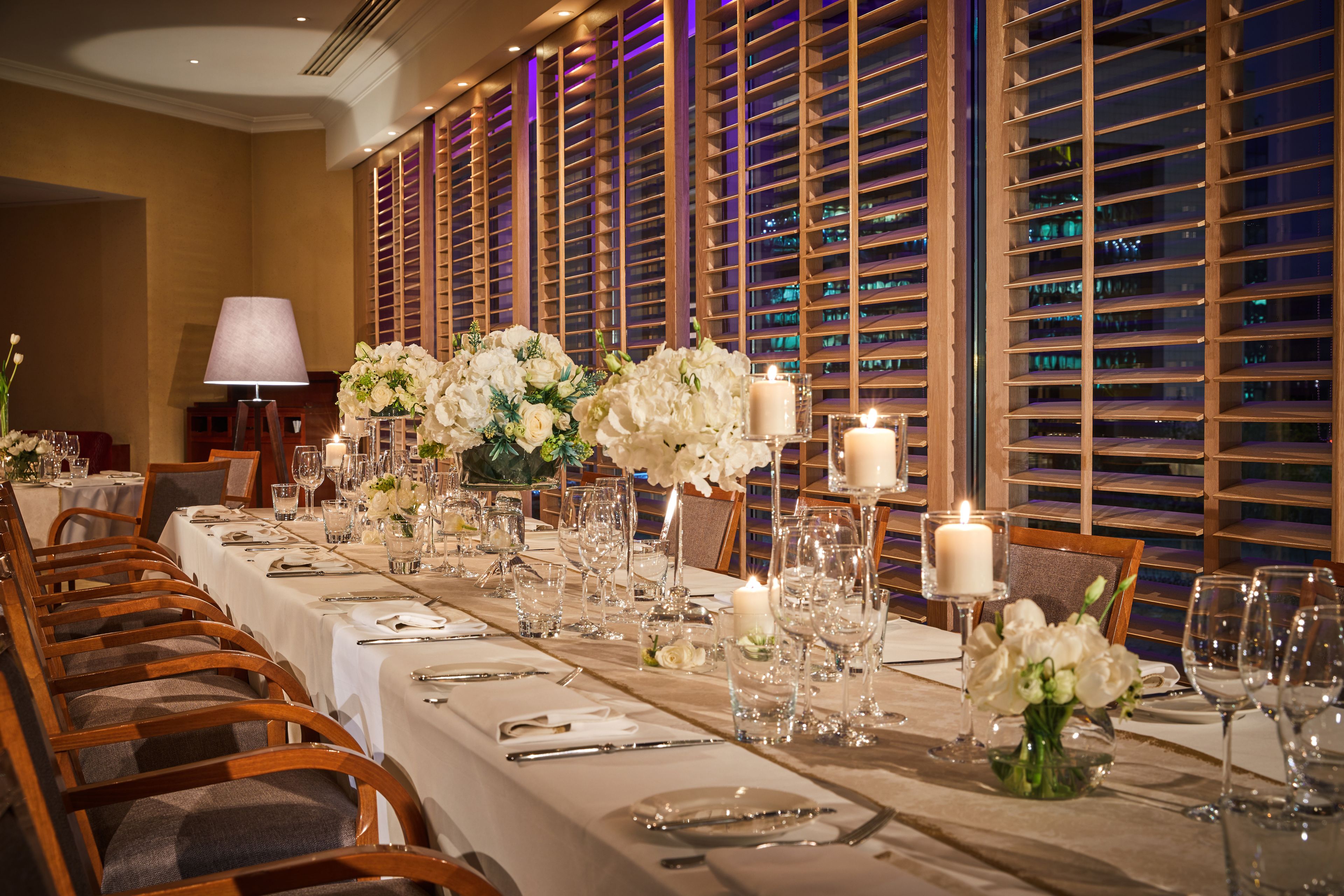 A long dining table set with white tablecloths, candles, and floral centerpieces.