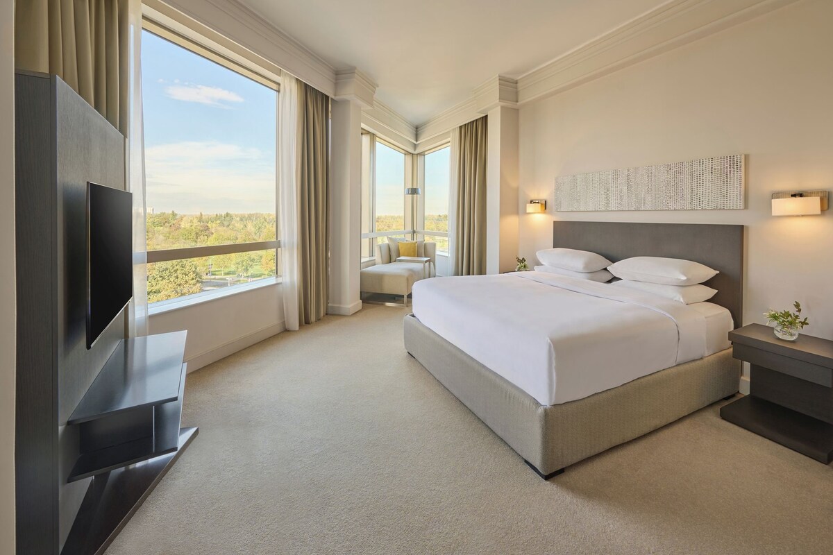 A hotel room with a large bed, a flat-screen TV, a desk, and a view of the outdoors.