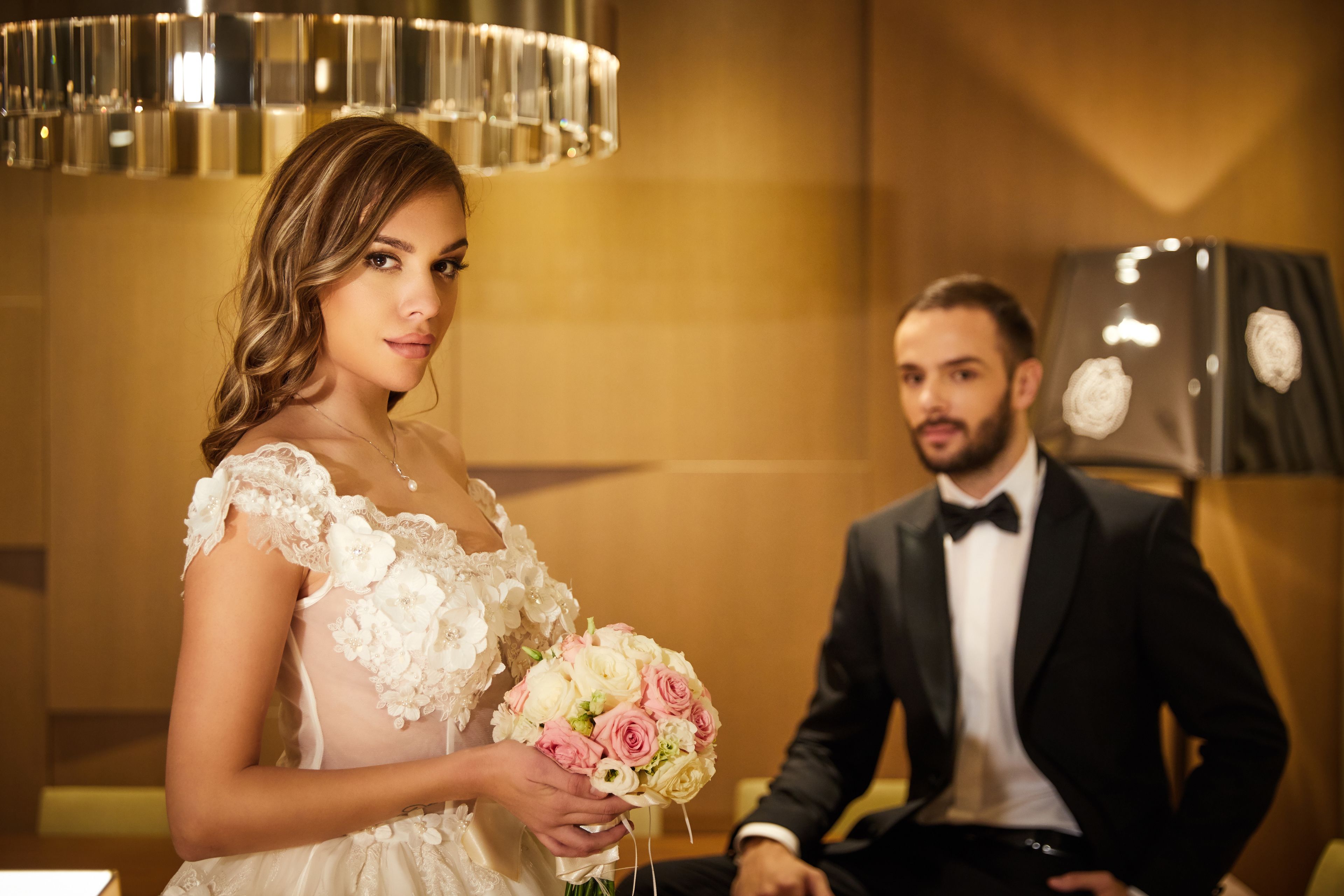 Cena de casamento com uma noiva segurando um buquê e um noivo de smoking.